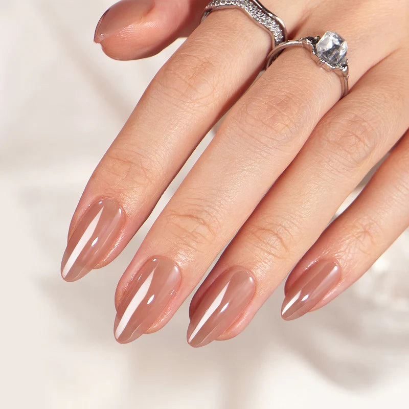 Close-up of a hand with nude nail polish and diamond rings on a light background