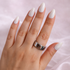 Hand with white nail polish and a silver ring on a light pink background